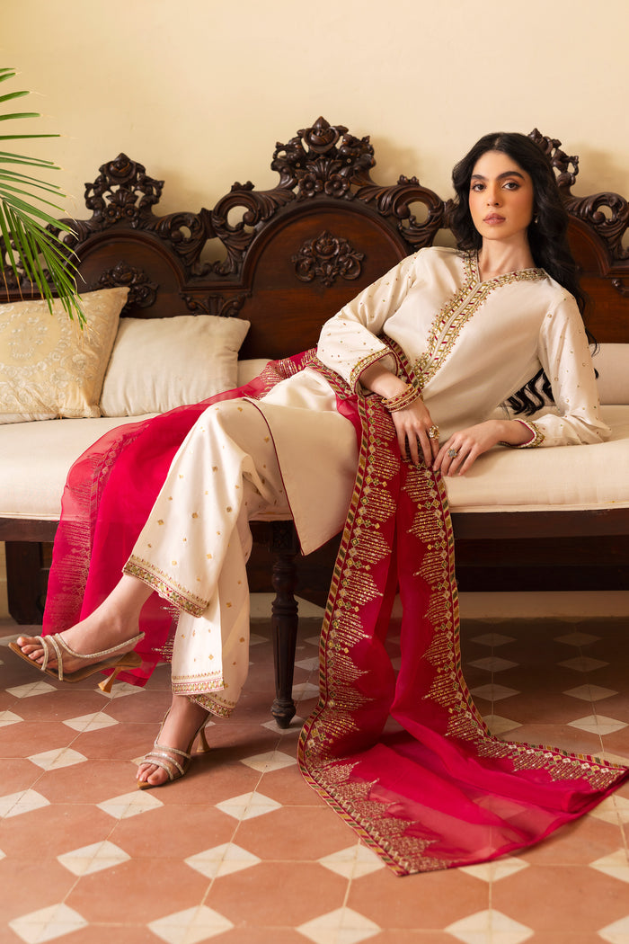 Model wearing full NAQSHI Abish 3PC set: embellished white raw‑silk shirt with V‑neck hand‑adda work, sequin-sprayed culottes & contrasting hot‑pink organza dupatta for a striking look.