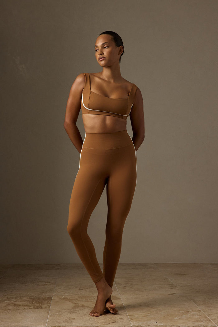 Three-quarter view of Acadia Legging in Caramel/Ivory on model showcasing high waist, doubled waistband and ivory side piping against a neutral studio background