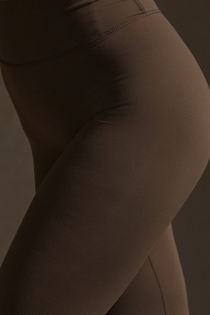 Side close-up of Acadia Legging in Stone Jersey showing high-rise waistband, smooth stretch fabric and flatlock seam on dark background