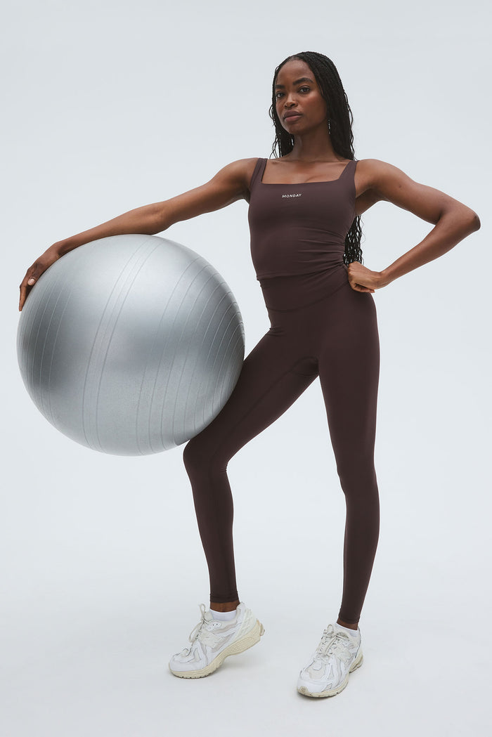 Full front view of Acadia Legging 27 inch in Espresso highlighting high waist and slim fit with silver exercise ball on light gray background
