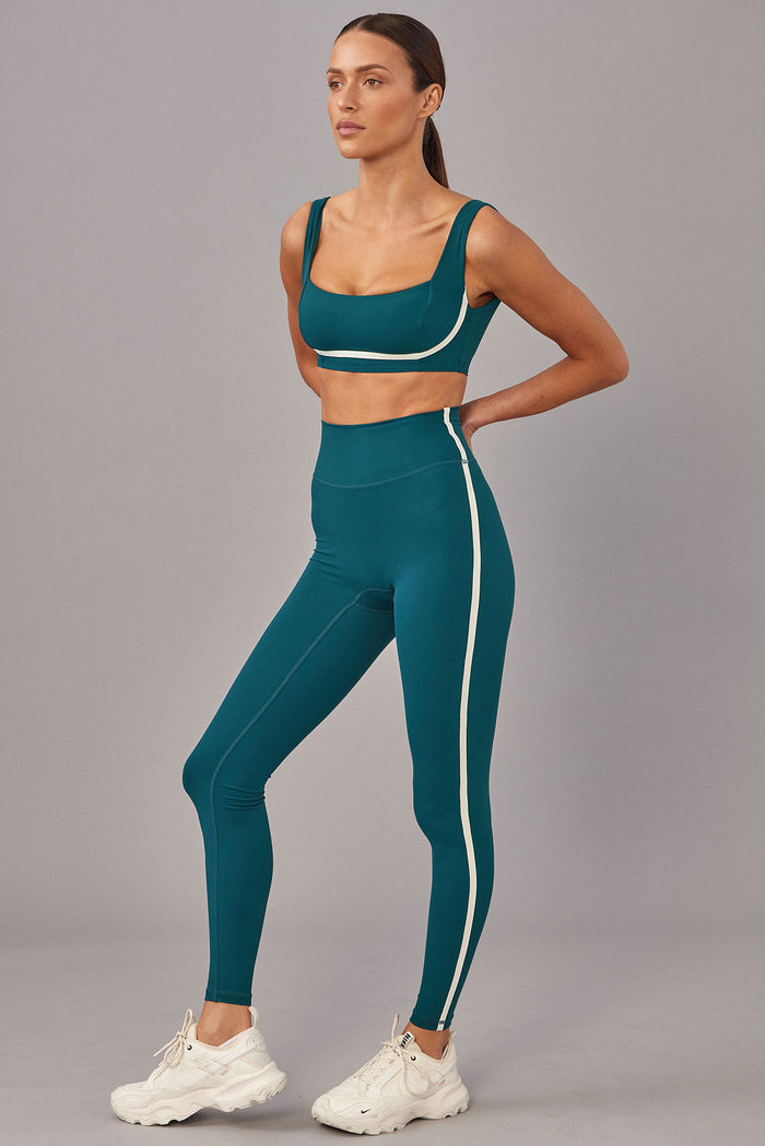 Three-quarter view of Acadia Legging 27 inch in Evergreen/Ivory with high-rise waist and ivory side stripe, paired with matching sports bra