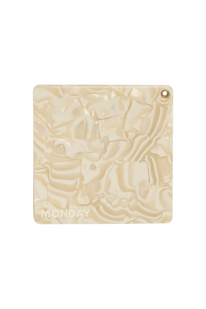 Close-up of Acklins Mirror (Ivory Swirl) showing marbled ivory panel with embossed MONDAY logo and brass grommet on white background