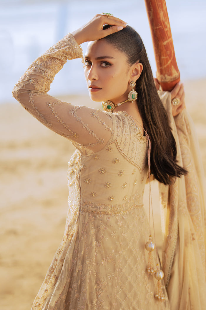 Model wearing full NAQSHI Alara 3PC set: skin‑beige net frock with hand‑embroidered tiers, heavy back tassels, plain straight PK raw‑silk pants and embellished dupatta.