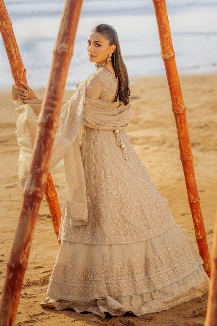 Model wearing full NAQSHI Alara 3PC set: skin‑beige net frock with hand‑embroidered tiers, heavy back tassels, plain straight PK raw‑silk pants and embellished dupatta.