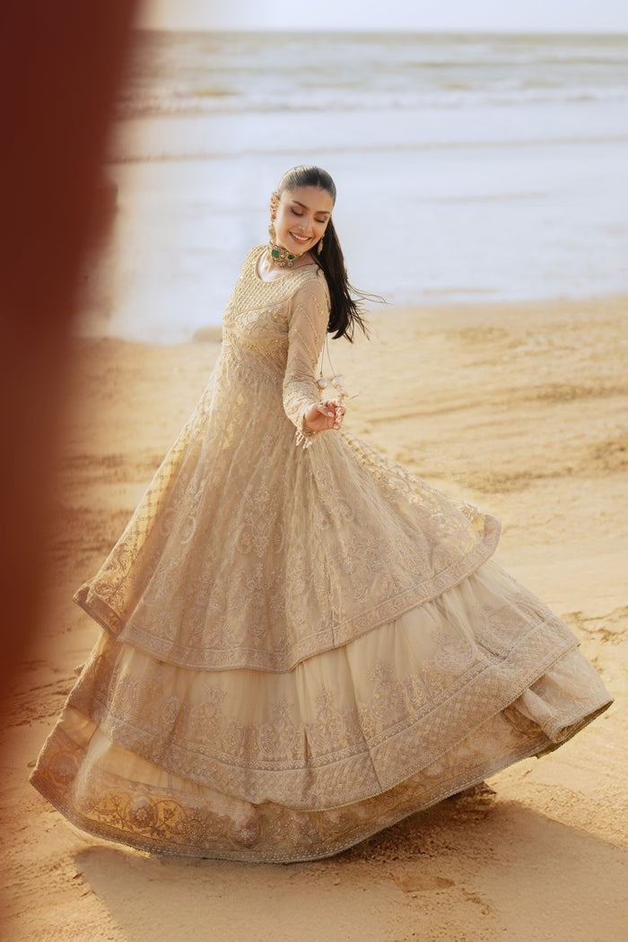 Model wearing full NAQSHI Alara 3PC set: skin‑beige net frock with hand‑embroidered tiers, heavy back tassels, plain straight PK raw‑silk pants and embellished dupatta.