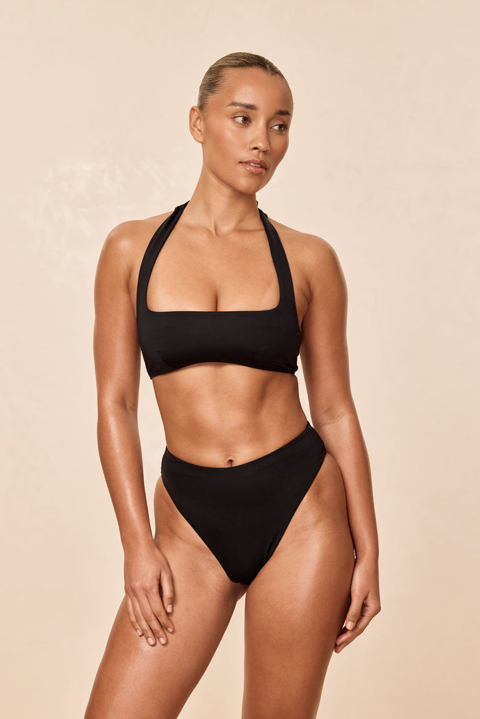 Three-quarter front of Amalfi Top in black showing square neckline and adjustable halter straps against a beige background