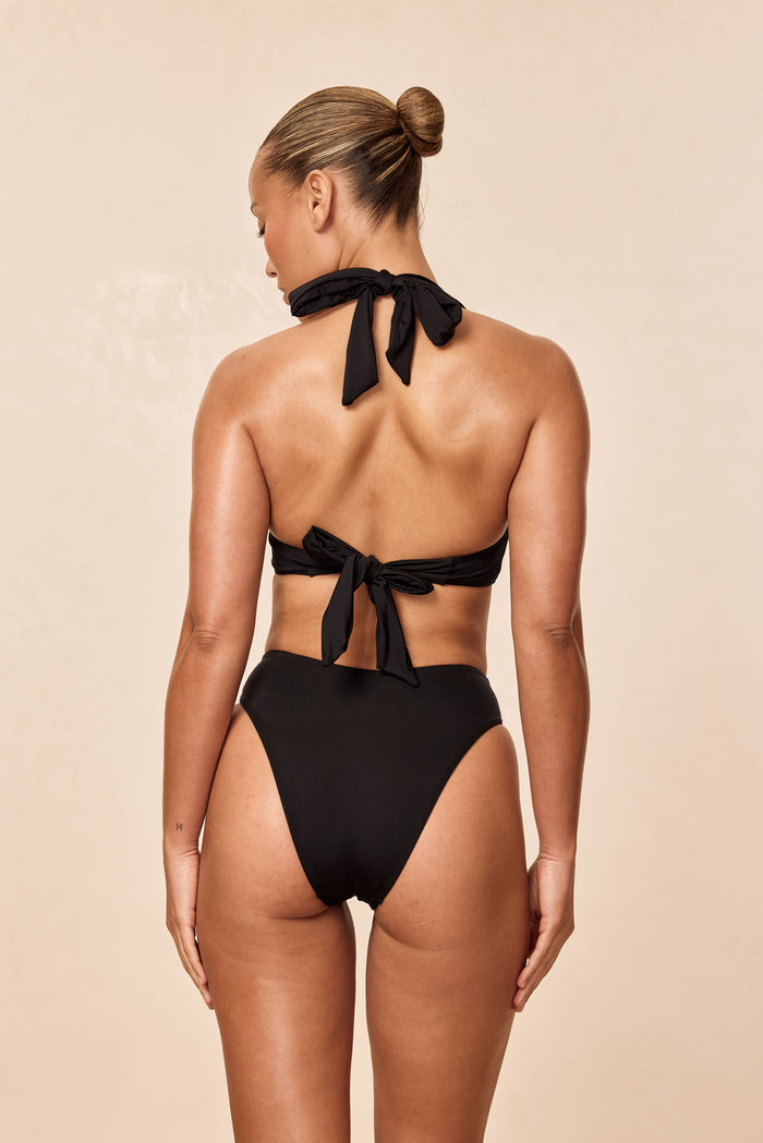 Back view of Amalfi Top in black showcasing tied halter and back bow on a neutral beige background