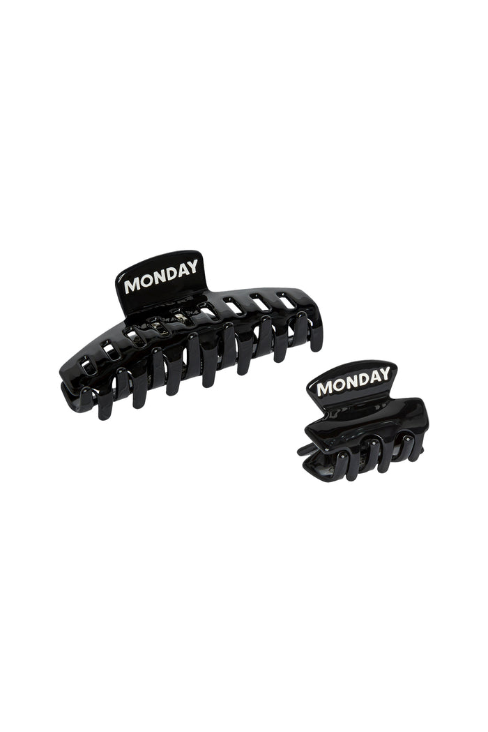 Angled flat lay of Angel Cay small and Staniel Cay medium black acetate clips showcasing engraved MONDAY logo on white background
