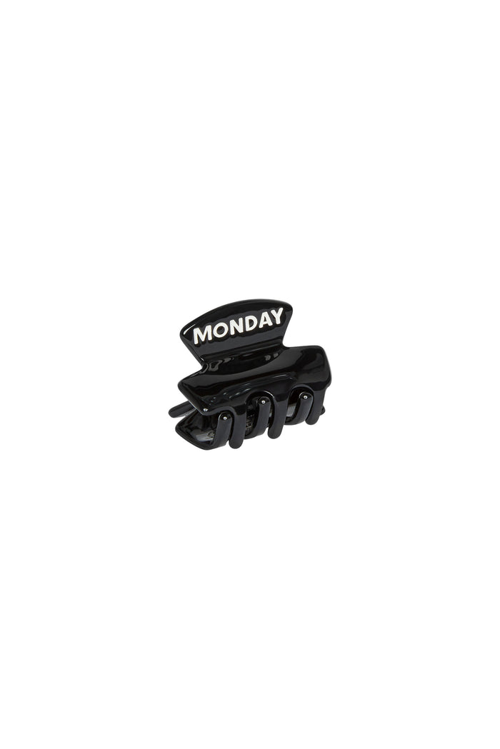 Black plastic hair claw clip with raised white letters reading MONDAY