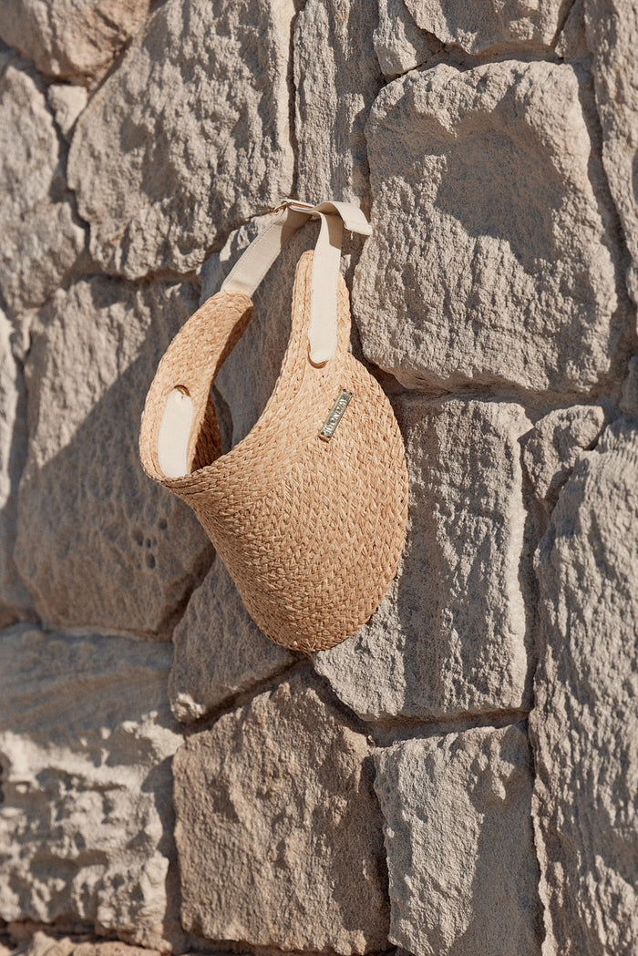 Close up of Anguilla Visor Natural with padded forehead, adjustable elastic band and gold Monday logo on sunlit stone wall