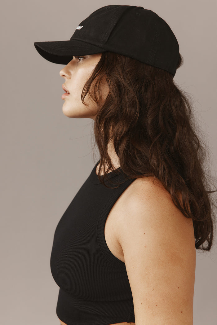 Profile view of Antigua Monday Cap in black on model showcasing curved brim and white MONDAY embroidery with neutral background