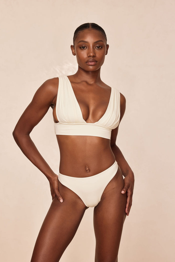Front view of Aruba Top in ivory showcasing pleated V-neck cups and underbust band on light beige background