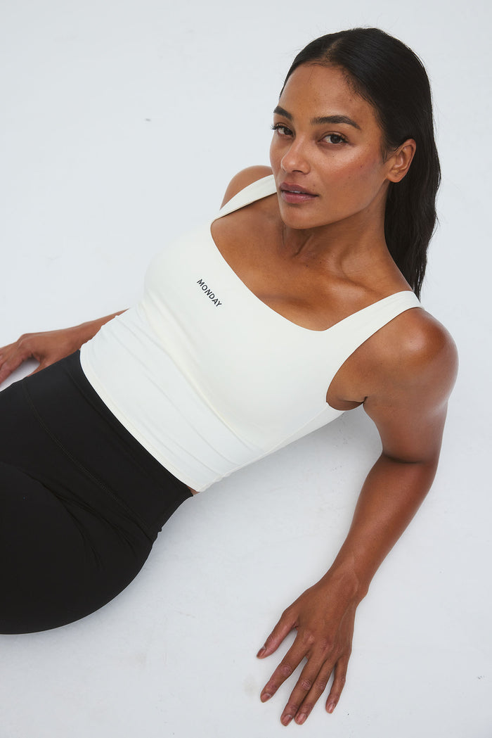 Reclining view of Aspen Tank in ivory with square neckline, shelf bra, cropped length and MONDAY logo on a white background