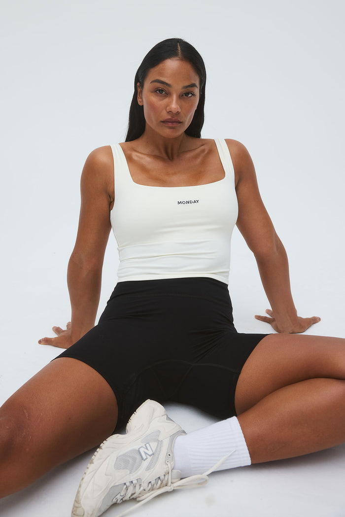Front view of Aspen Tank in ivory showcasing square neckline, MONDAY chest logo, and cropped length on model against white background