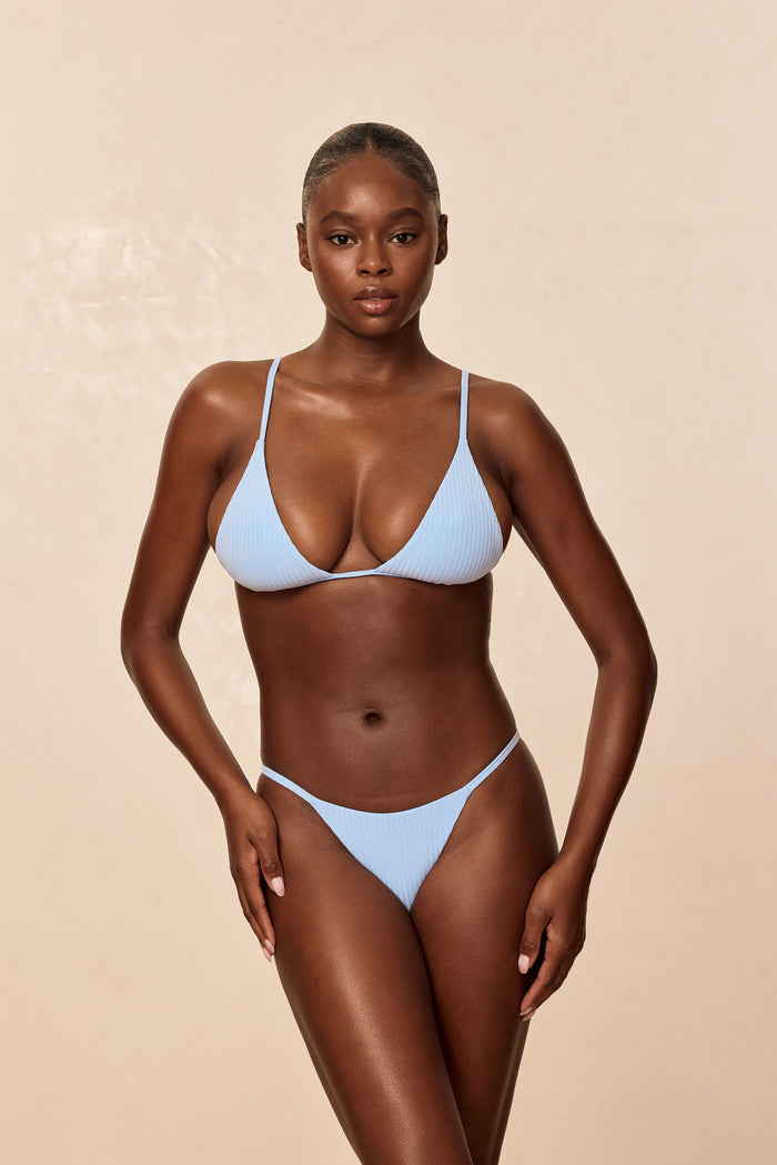 Front of Barbados Bottom in Sky Rib, high-cut leg, thin side straps and minimal coverage on model, beige background