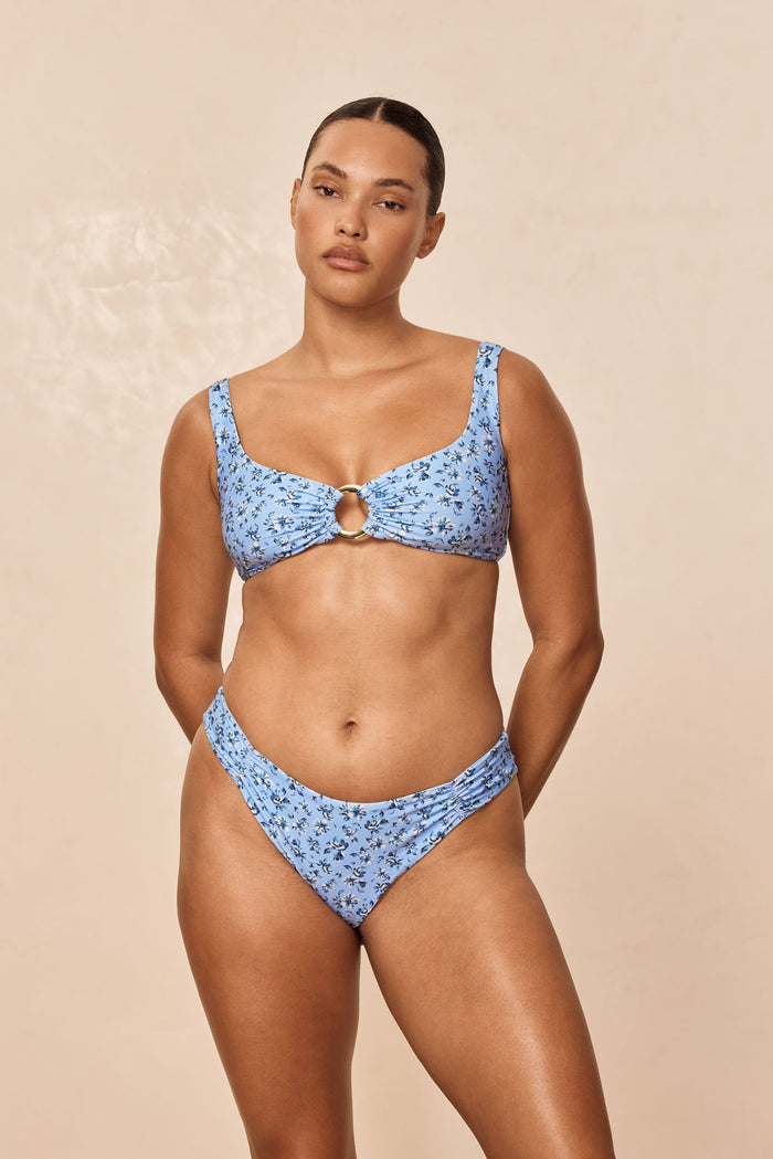 Front view of Barbuda Top in Isola Floral on model showcasing center gold ring, over-the-shoulder straps, beige background