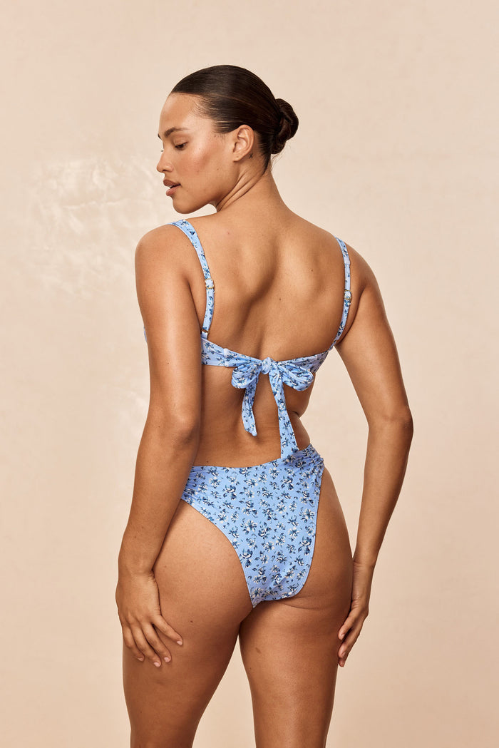 Back view of Barbuda Top in Isola Floral with adjustable back tie, shoulder straps, blue floral print, beige backdrop