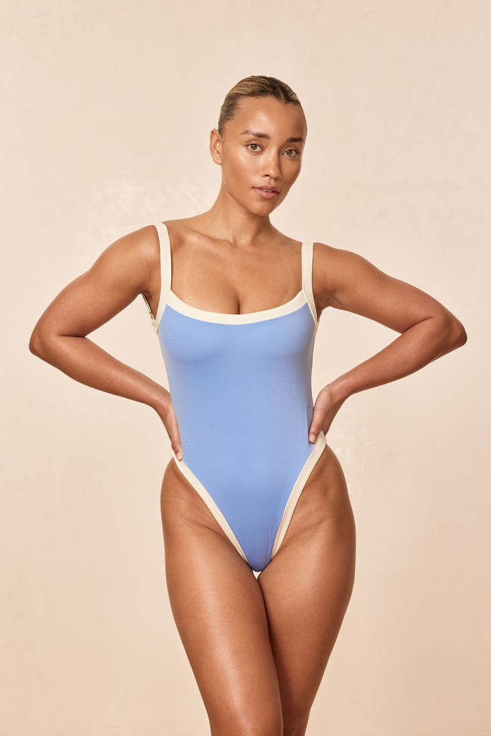 Front view of Barcelona One Piece in azure with ivory trim showing high-cut leg and scoop neckline on beige background