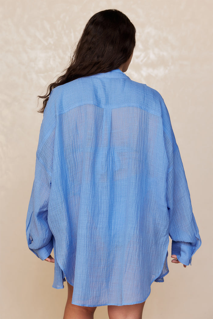 Back view of Barcelona Tunic in Azure crinkle linen showcasing semi-sheer crinkle texture and oversized relaxed fit on a beige studio backdrop
