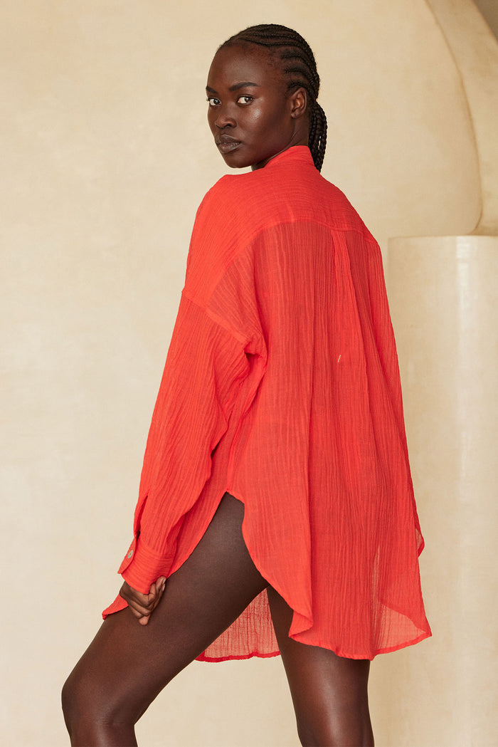 Rear three-quarter view of Barcelona Tunic in Chili Pepper crinkle linen showcasing sheer, oversized fit with high-low hem against a beige backdrop
