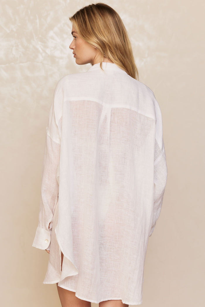 Back view of Barcelona Tunic in white showing sheer linen fabric, center back yoke, and buttoned cuff on beige backdrop