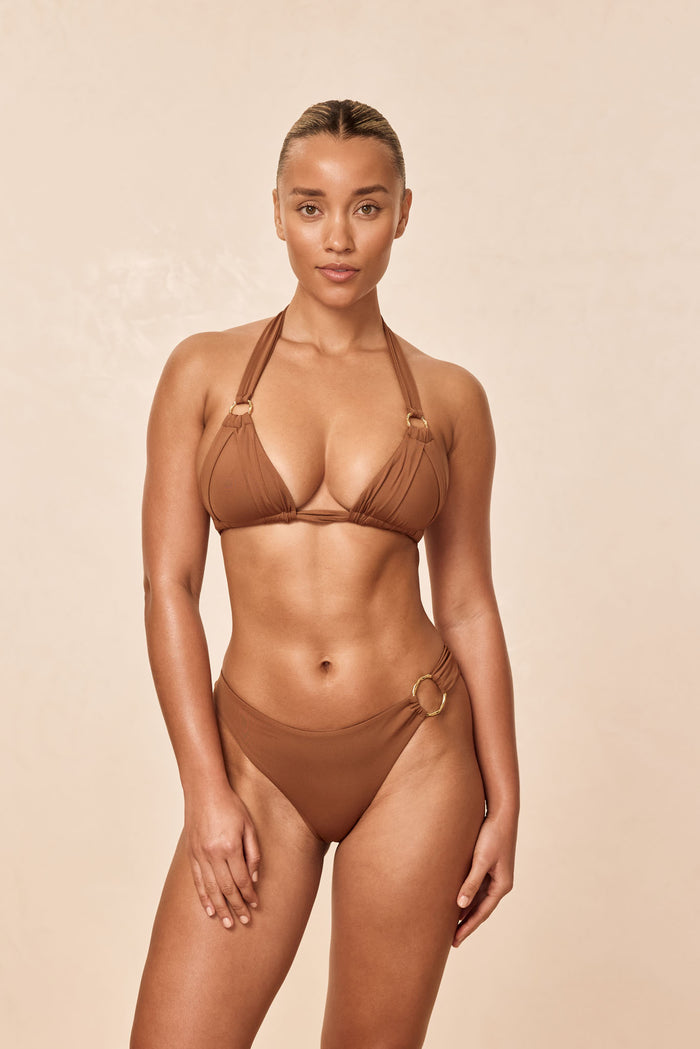 Front view of Bari Top in Caramel on model showing pleated cups, adjustable ties, and gold rings on beige background