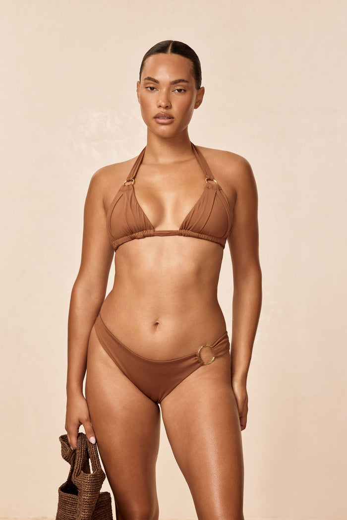 Front of Bari Top in Caramel with pleated cups, gold ring detail and adjustable halter ties on model, beige background