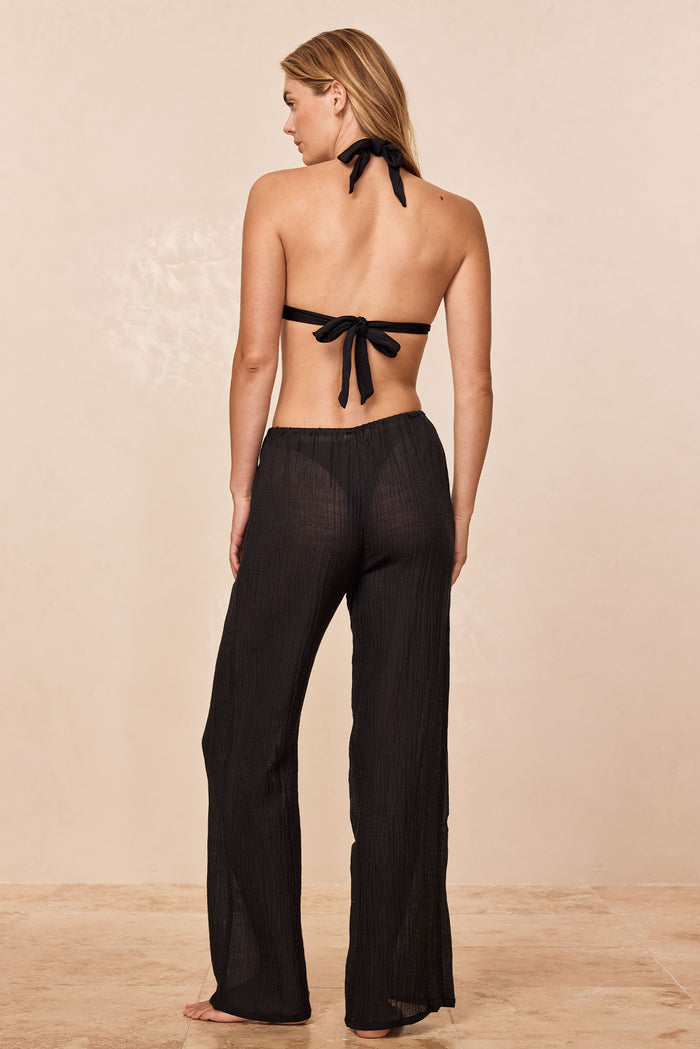 Back view of Belize Pant in Black Crinkle Linen showing sheer wide-leg silhouette and elastic waistband on beige studio floor