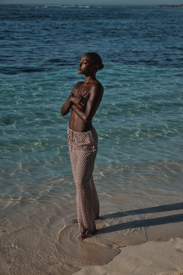 Three quarter view of Belize Pant Husk Geo linen with relaxed fit and drawstring waist on model in shallow ocean