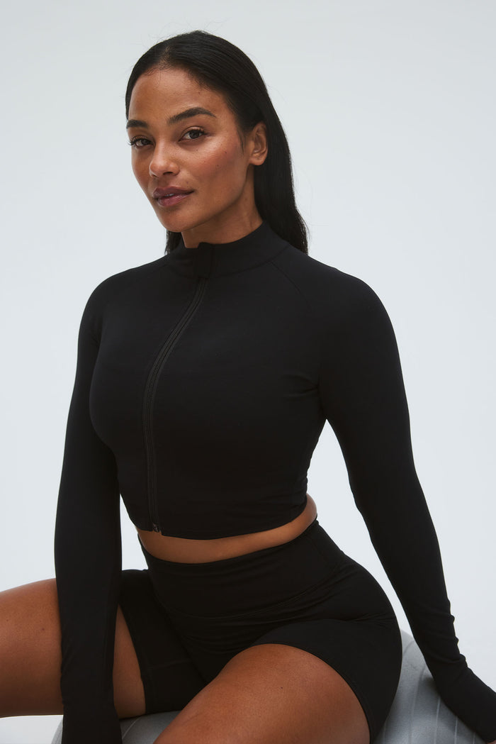 Three quarter front of Big Sur Jacket in black showing mock neck, center zipper and thumbhole sleeves on neutral background