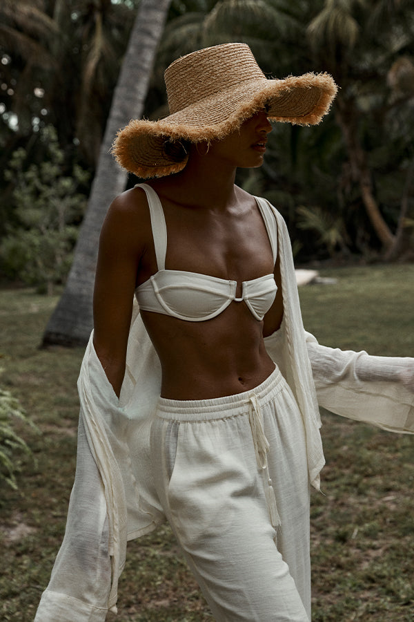 Three-quarter view of Bondi Hat - Small Brim straw hat on model showcasing 4 1/2 inch frayed brim with palm trees in background