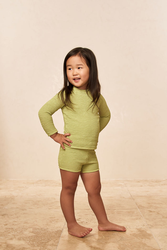 Three-quarter view of Bondi Rashguard Kids in Avocado Crinkle showcasing textured crinkle fabric and matching shorts on a neutral studio background