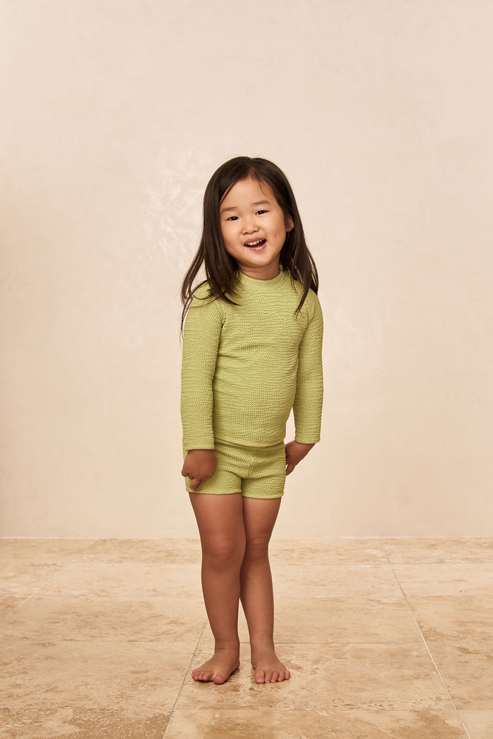 Front view of Bondi rashguard kids avocado crinkle long-sleeve with matching shorts on beige studio floor