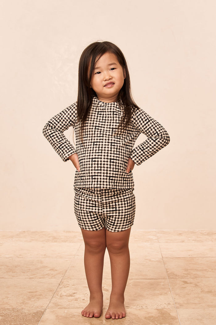 Front view of Santa Cruz Short Kids in black gingham showcasing mid-thigh shorts and matching long-sleeve top on beige tiled floor