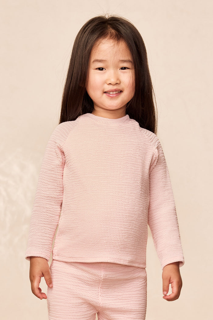 Front view of Bondi Rashguard Kids in Powder Pink Crinkle showing long sleeves and crinkle texture on beige background