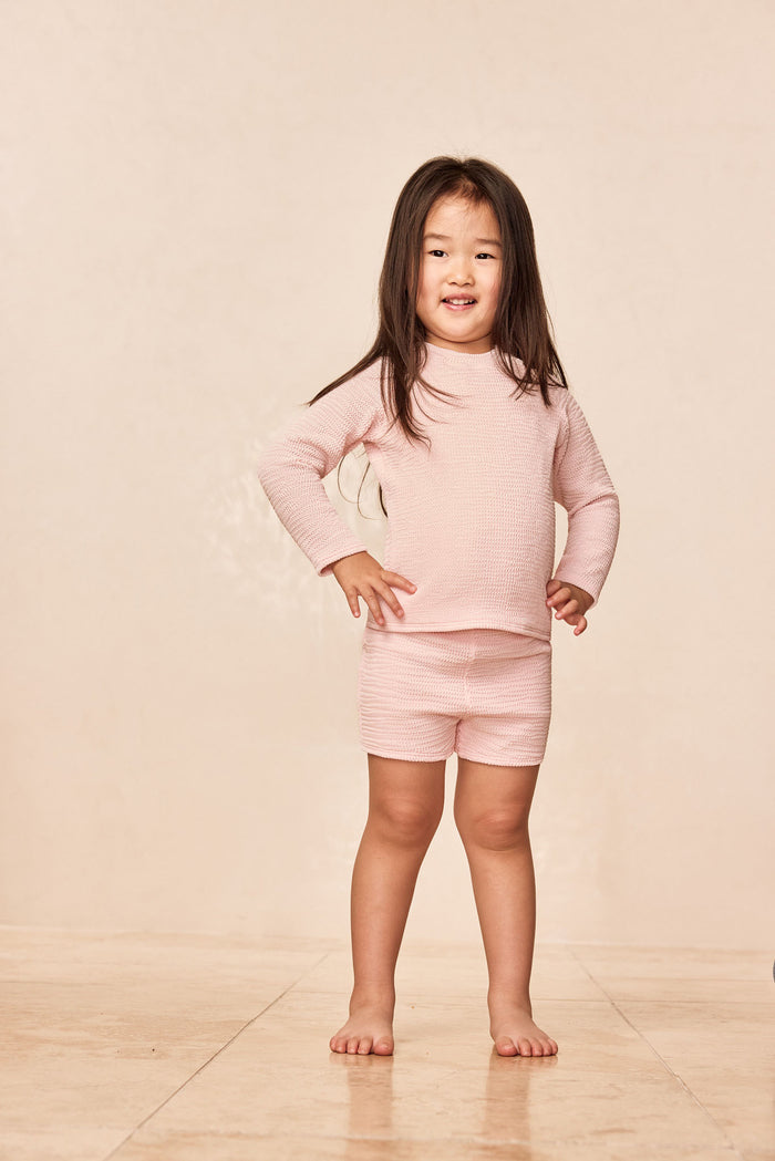 Front view of Bondi Rashguard Kids in Powder Pink Crinkle with crinkle texture and long sleeves on child model against neutral backdrop