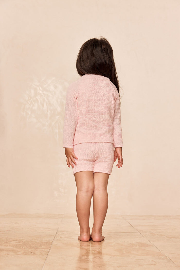 Back view of Bondi Rashguard Kids in powder pink crinkle showing textured long-sleeve top and matching shorts