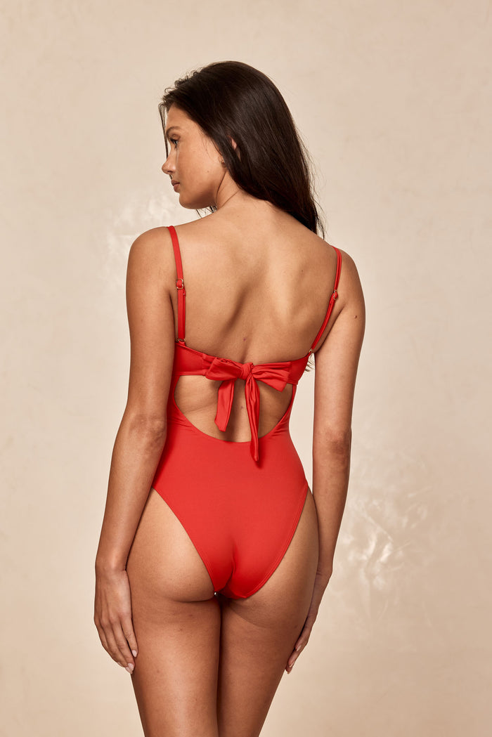 Back view of model wearing a red one-piece swimsuit with tied bow at back and adjustable shoulder straps