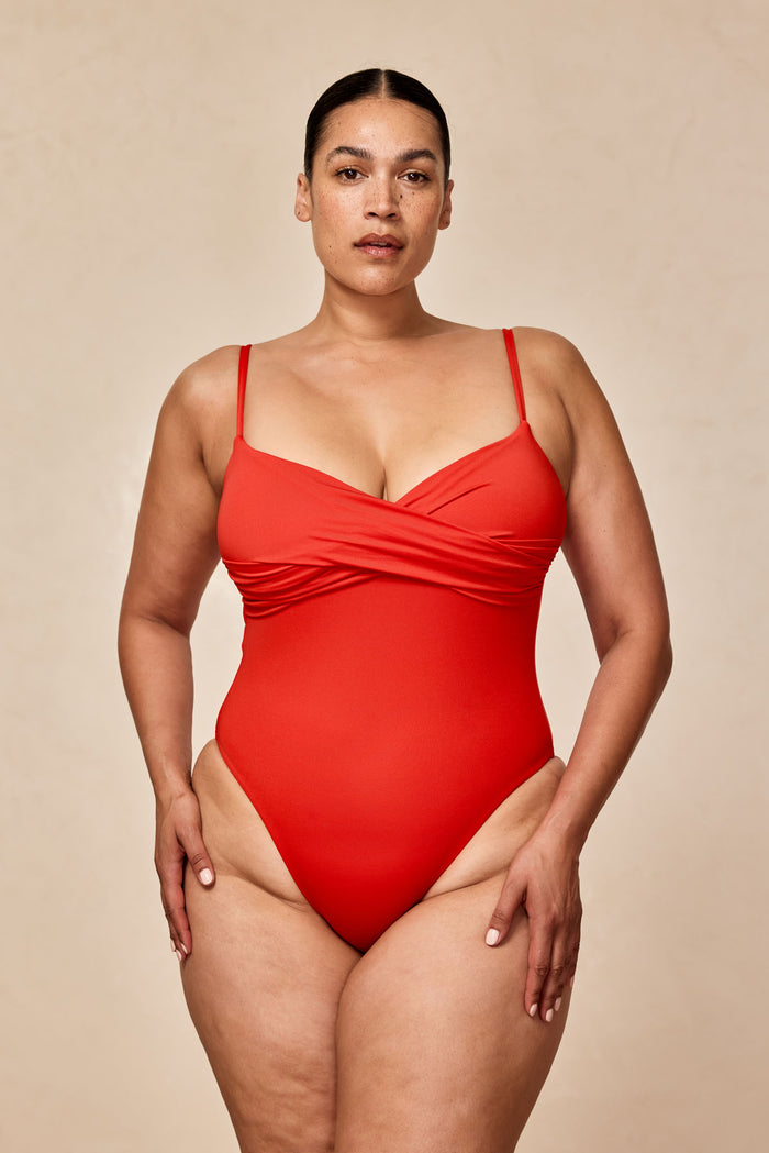 Front view of person in a red one-piece swimsuit against a neutral beige background.