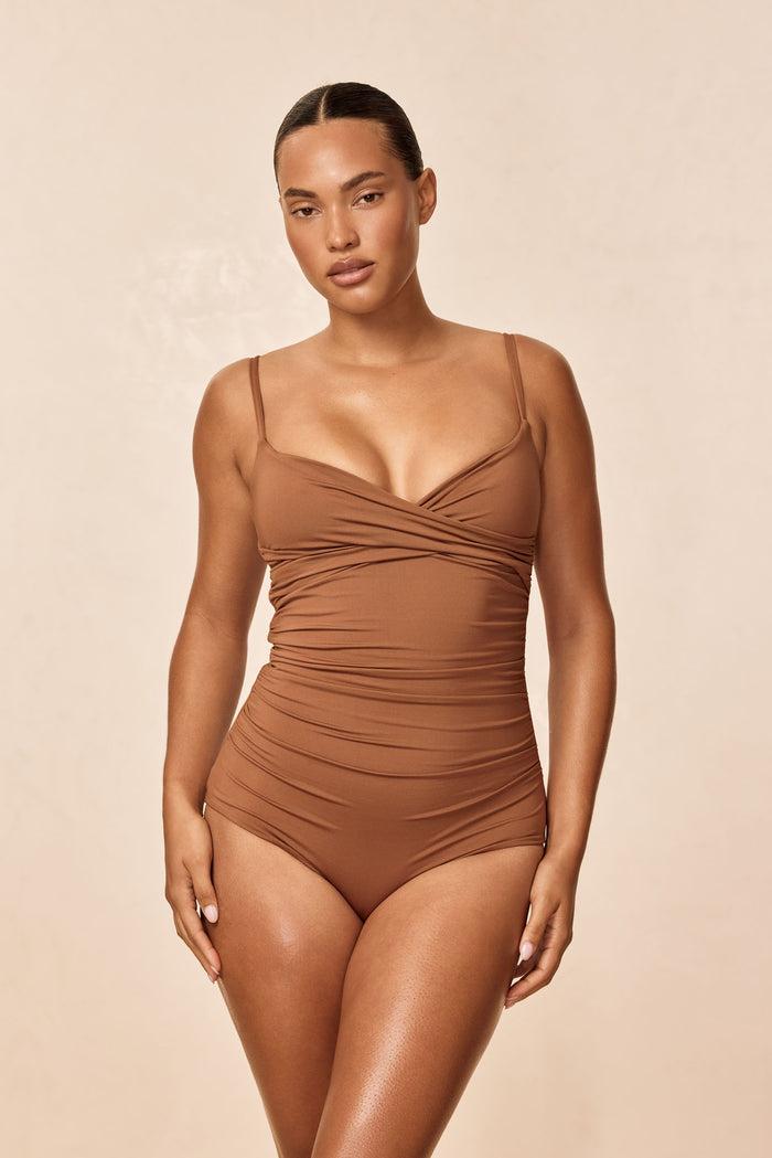 Front view of Bordeaux one-piece in caramel showing crossover neckline, adjustable straps and ruched full coverage on model