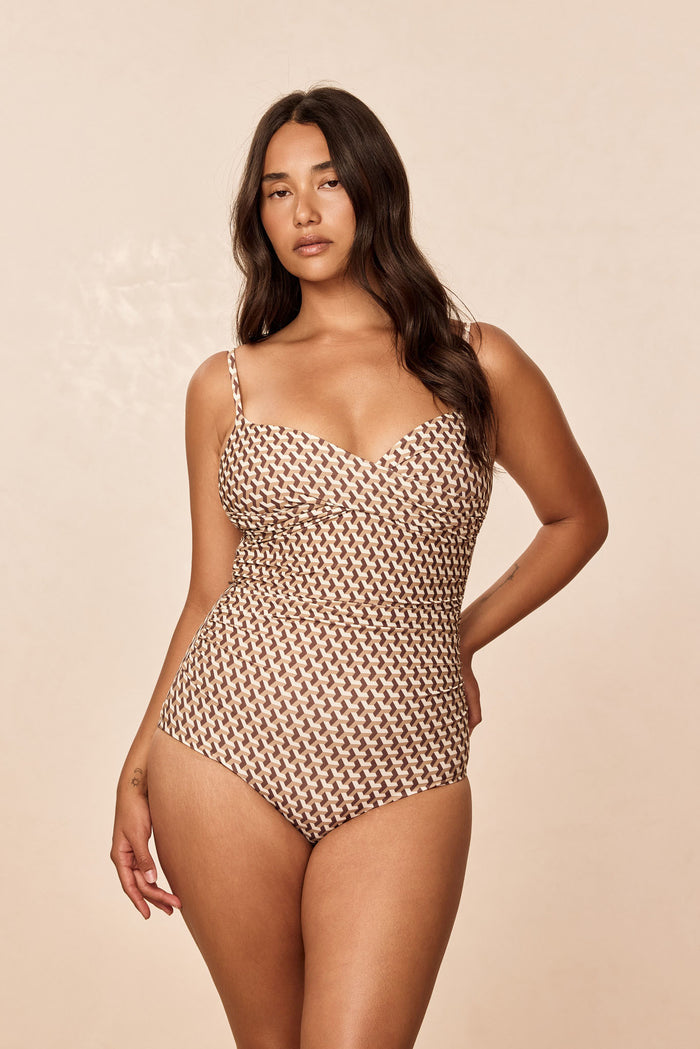 Three-quarter front of Bordeaux one-piece Husk Geo, crossover neckline, adjustable straps and ruching on beige backdrop
