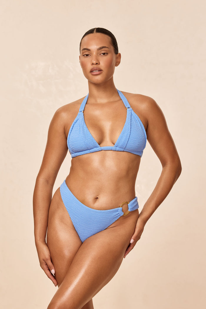 Three-quarter front of Bronte Bottom in Azure Crinkle showcasing high-cut leg and gold side ring on a beige studio background