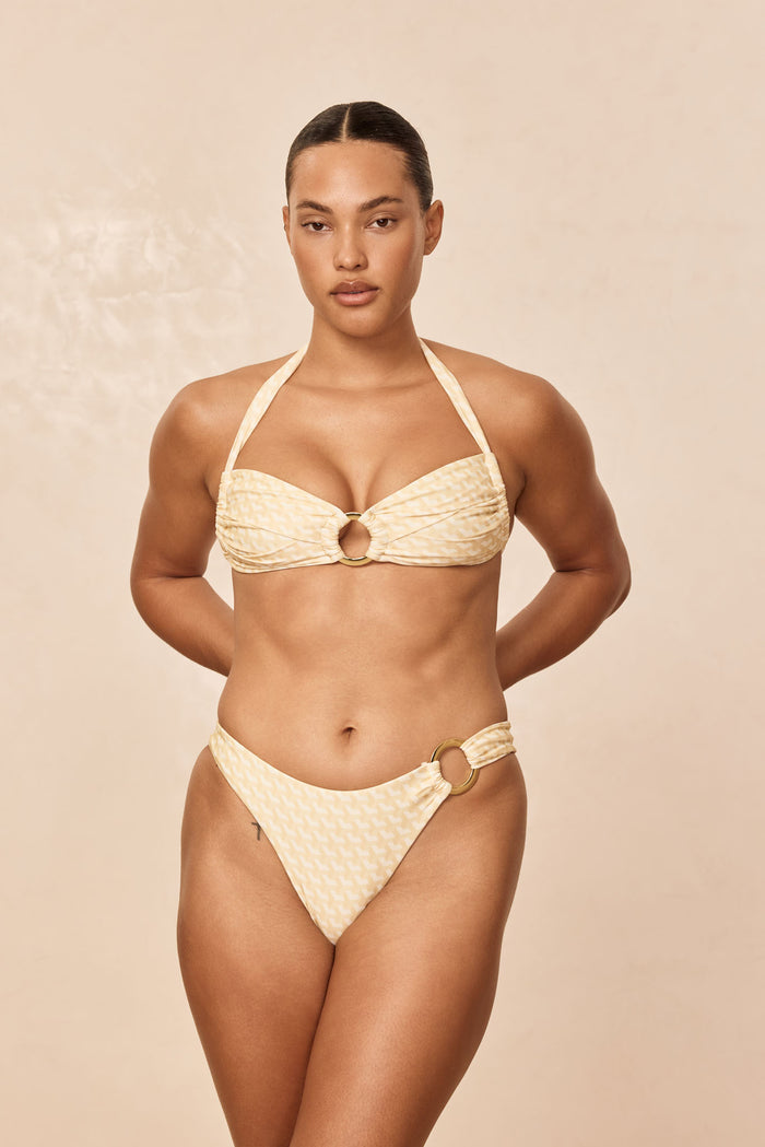 Front view of Bronte Top Ivory Geo on model, bandeau with gold center ring, pleating and halter tie, neutral backdrop