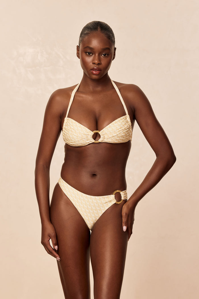 Front view of Bronte Top in Ivory Geo on model, bandeau shape with gold center ring and pleated detail, beige background