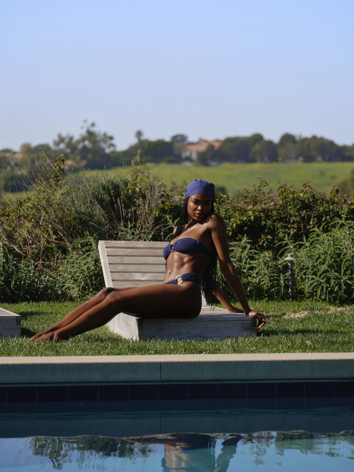 Seated model wearing Costa Rica Top in Midnight Crinkle, bandeau with removable halter and adjustable back tie by a pool