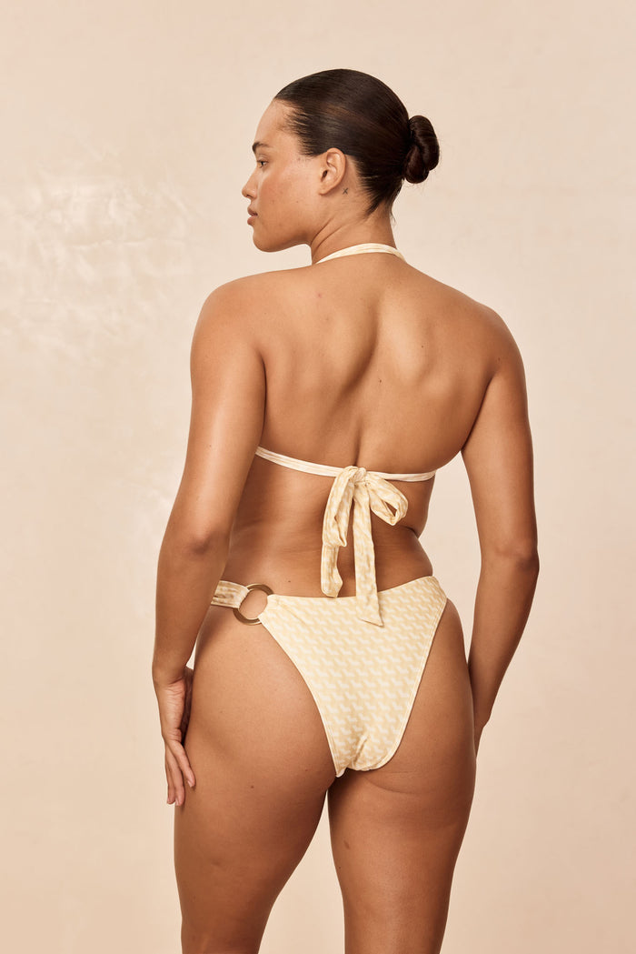 Rear view of Bronte Top in Ivory Geo on model showing adjustable halter neck and tied back closure against beige background
