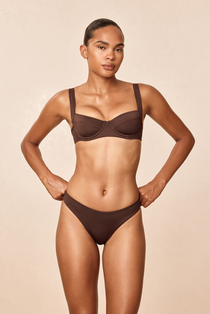 Front view of Byron Bottom in espresso on model, mid-rise high-leg cut showing fit and ribbed fabric against a beige background