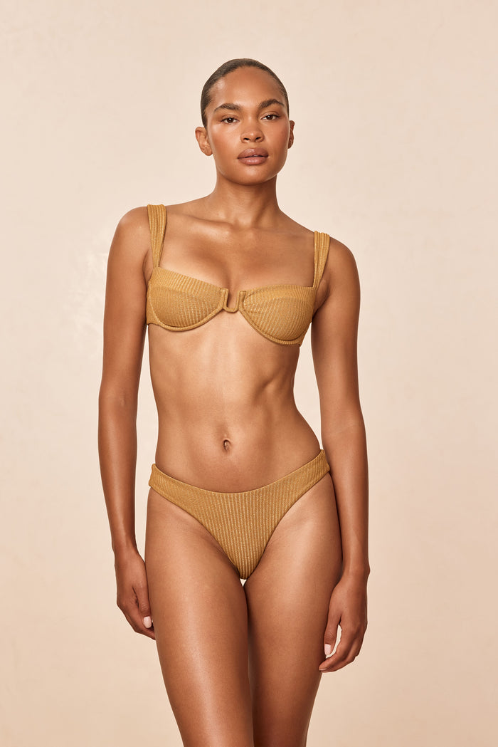Front view of Cala Roja Top in antique gold lurex rib showing underwire balconette cups and ribbed shimmer on beige background
