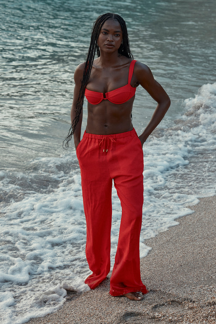 Three-quarter front of Cala Roja Top in Chili Pepper showing underwire balconette cups and U-shaped center with model at water’s edge