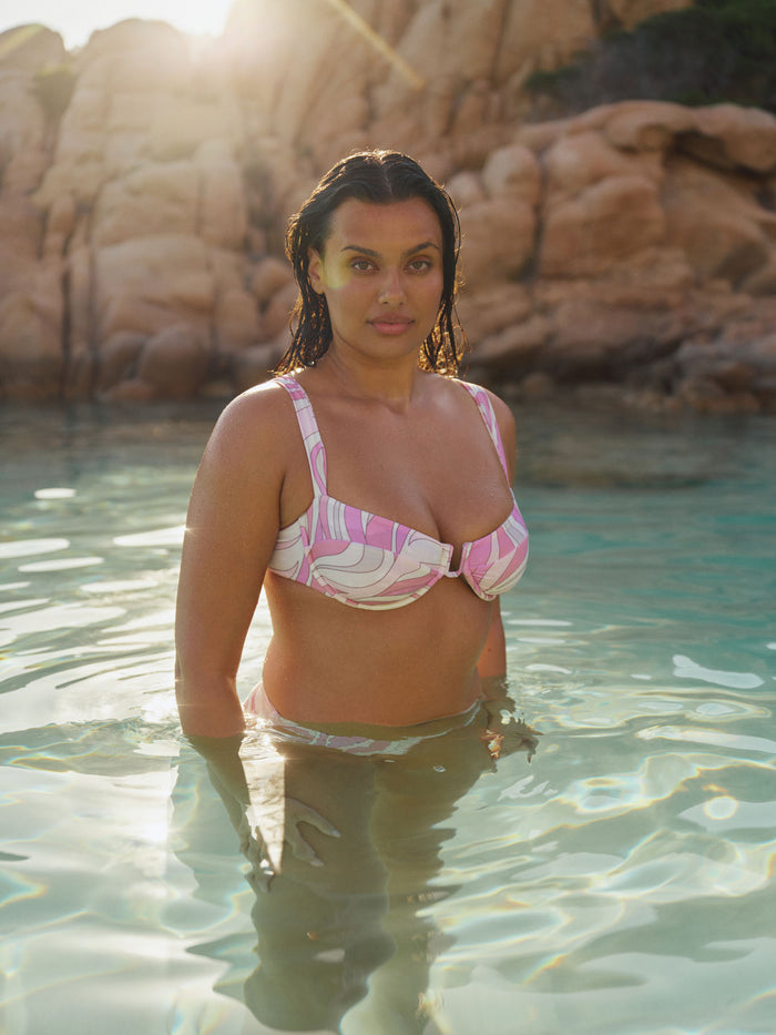 Front waist up view of Cala Roja Top in Costa Rei Pink showing underwire cups, soft u wire detail and wide shoulder straps on a model in shallow water